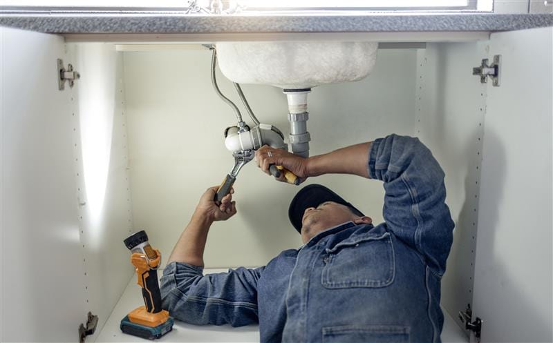 Plumber repairing pipes beneath a bathroom sink in Lancaster