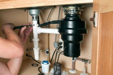 Plumber repairing a garbage disposal beneath a kitchen sink in Lancaster
