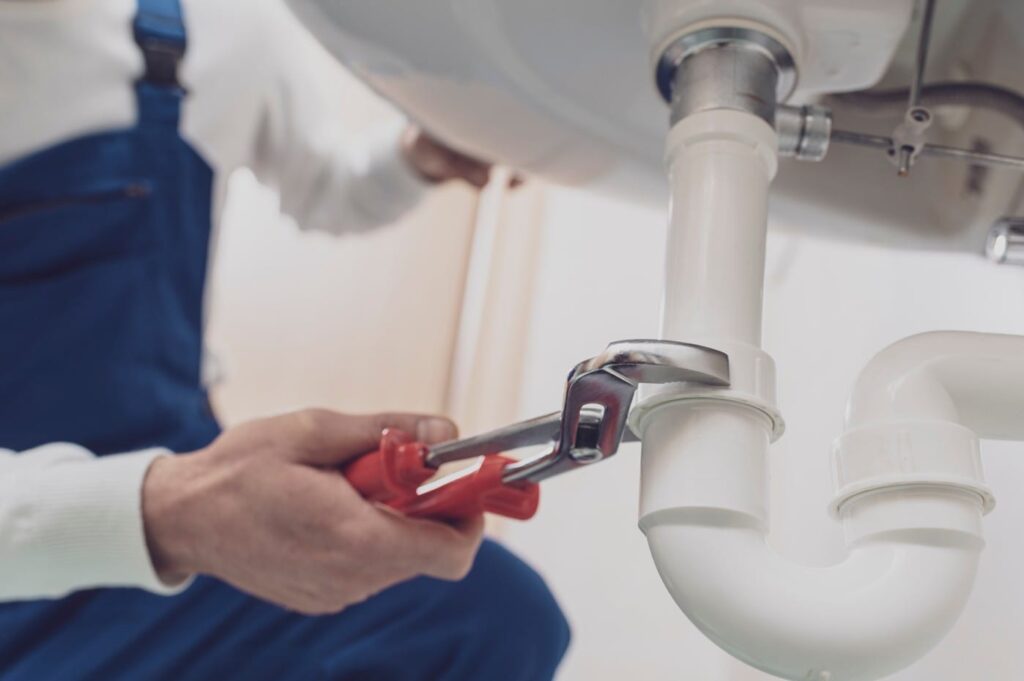 Plumber repairing a white drain pipe beneath a sink in Lancaster